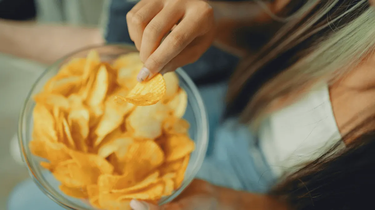 Frau mit Chipstüte auf dem Sofa – Symbol für emotionales Essen und Kontrollverlust beim Snacken