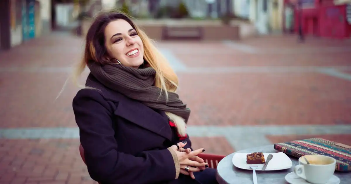 Lachende Frau sitzt mit Kaffee und einem Stück Kuchen in einem Straßencafé